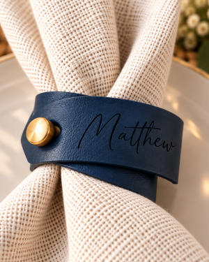 Indigo faux leather napkin ring engraved with Matthew and finished with a gold button on a white wedding napkin